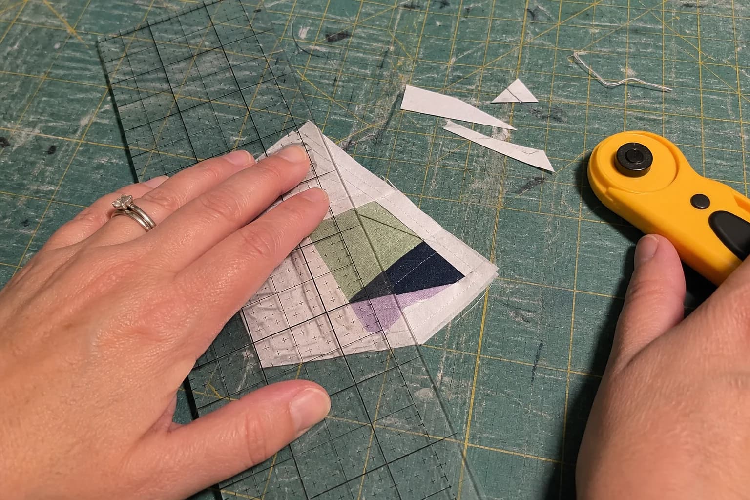 A foundation paper pieced section is aligned under a clear ruler before its seam allowance is trimmed.