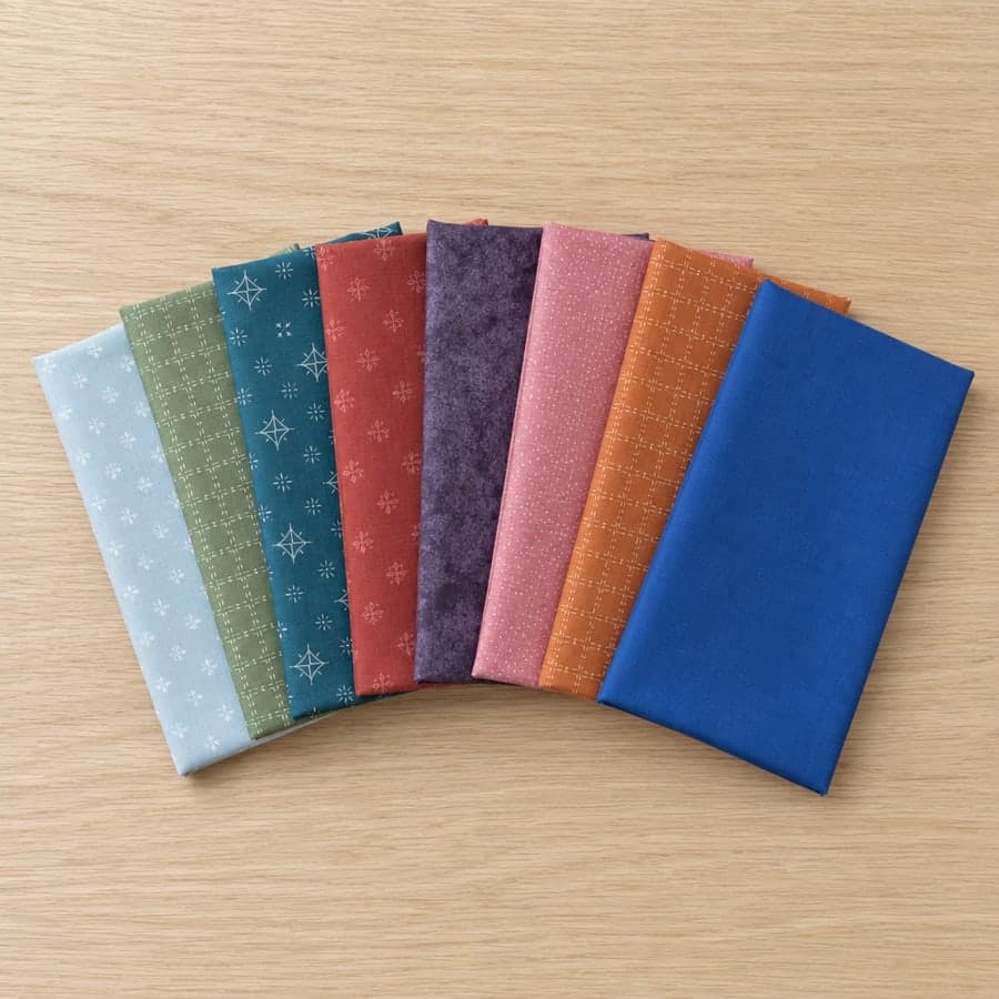 Eight folded fat quarters fanned out on a pale oak board — red, hot pink, orange, cobalt blue, teal, plum, sage green and a pale ice-blue print.