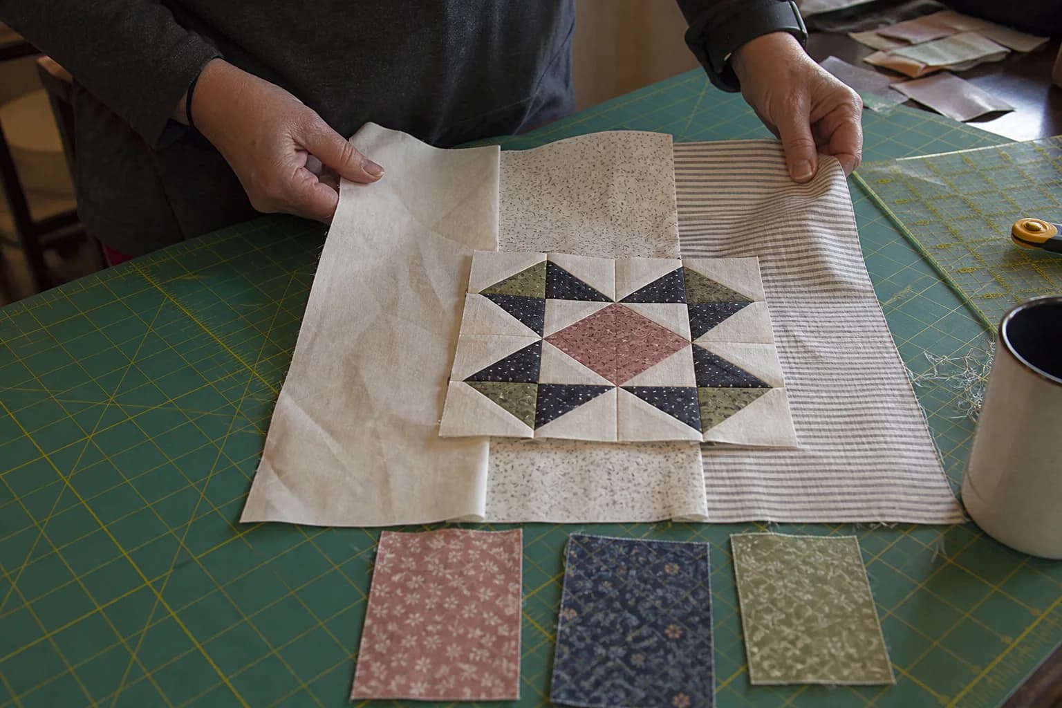 A quilter auditions cream, low-volume, and striped backgrounds behind a small patchwork block.
