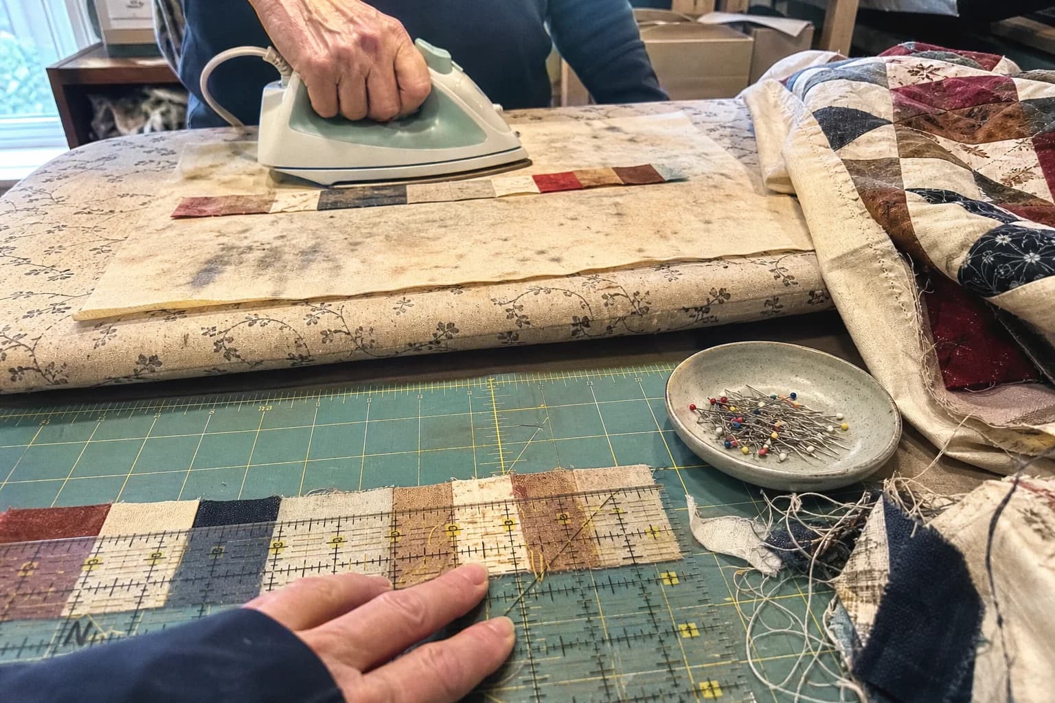 A quilter presses a patchwork seam while checking a sewn strip against a clear ruler.