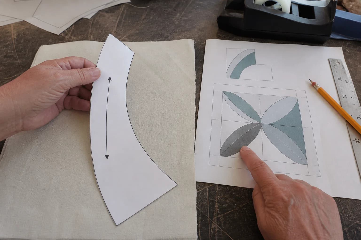 A curved paper quilt template sits beside pattern pages, fabric, scissors, and pencil notes.
